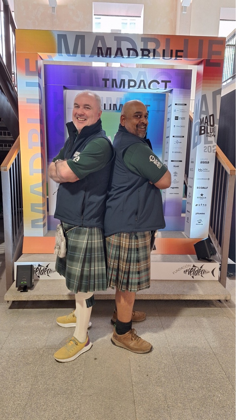 Two men standing back to back wearing kilts